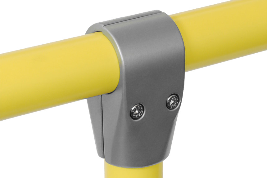 Un conector en T gris de metal une dos tubos amarillos. Un tubo horizontal pasa por la parte superior, mientras que uno vertical se une desde abajo. Se ven dos tornillos plateados en la parte delantera. Fondo blanco liso.